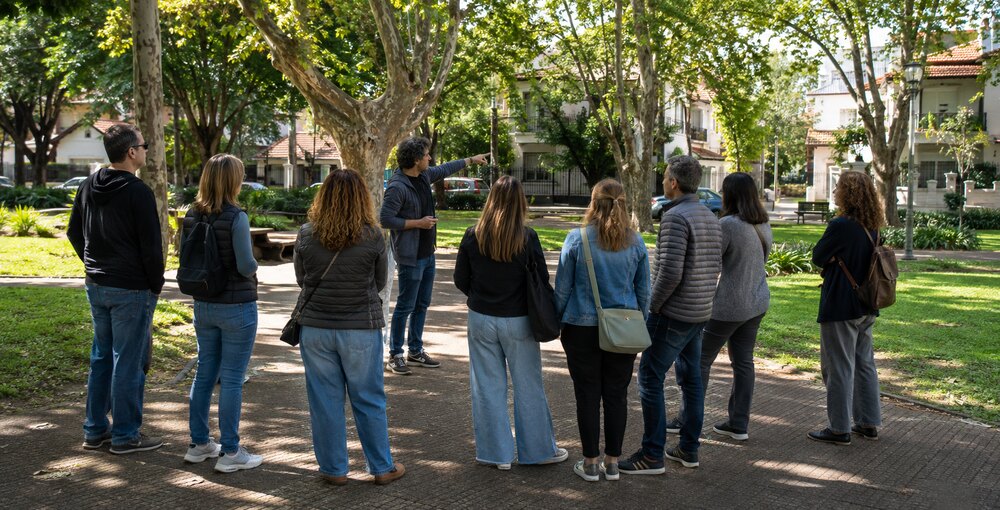 Grupo de visitantes ficticios escucha las explicaciones de un guía durante un recorrido cultural por la plaza Ciudad de Banff, en Versalles.
